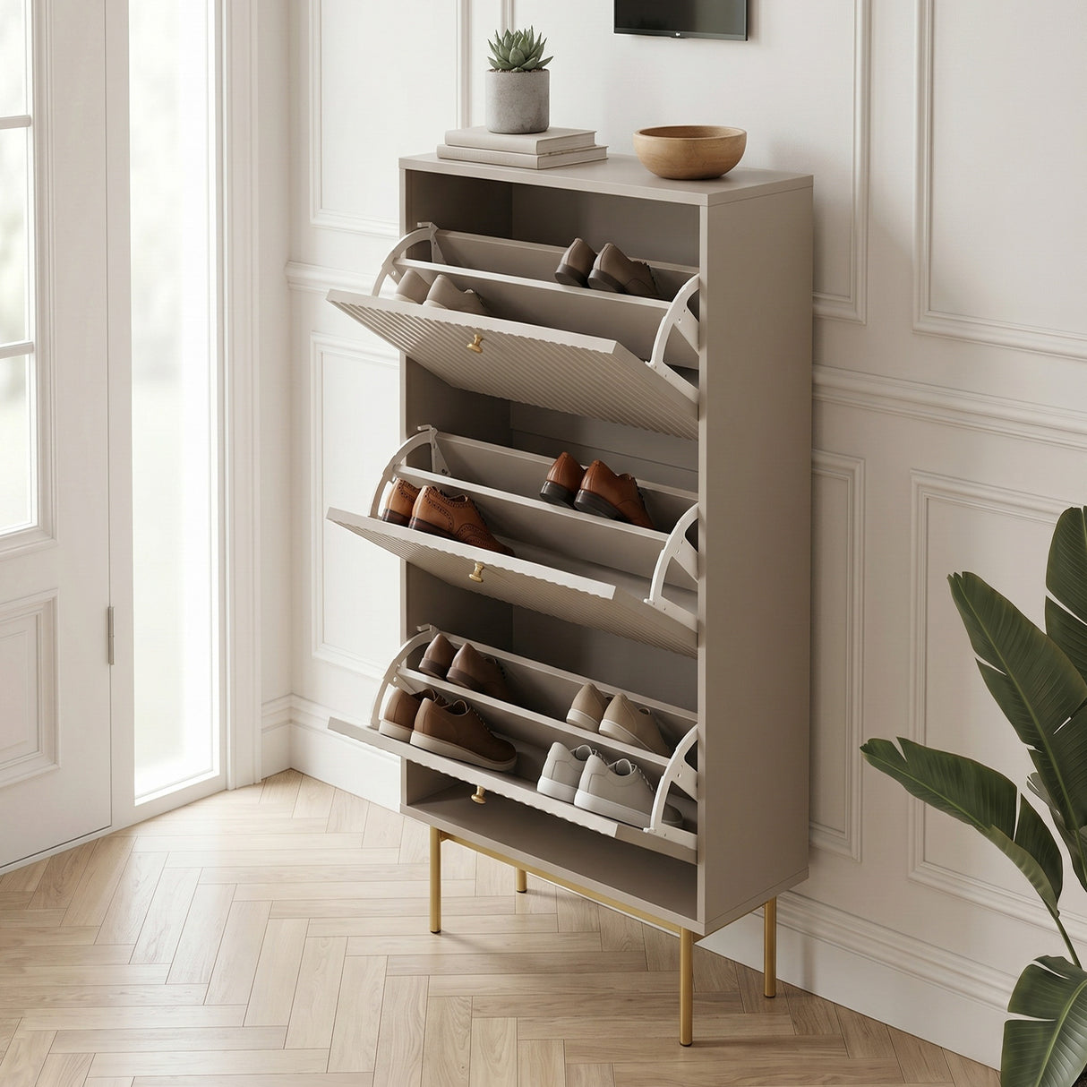 Beige Devon Shoe Cabinet with three open tilt out compartments, gold handles and legs, styled with shoes in a bright hallway.