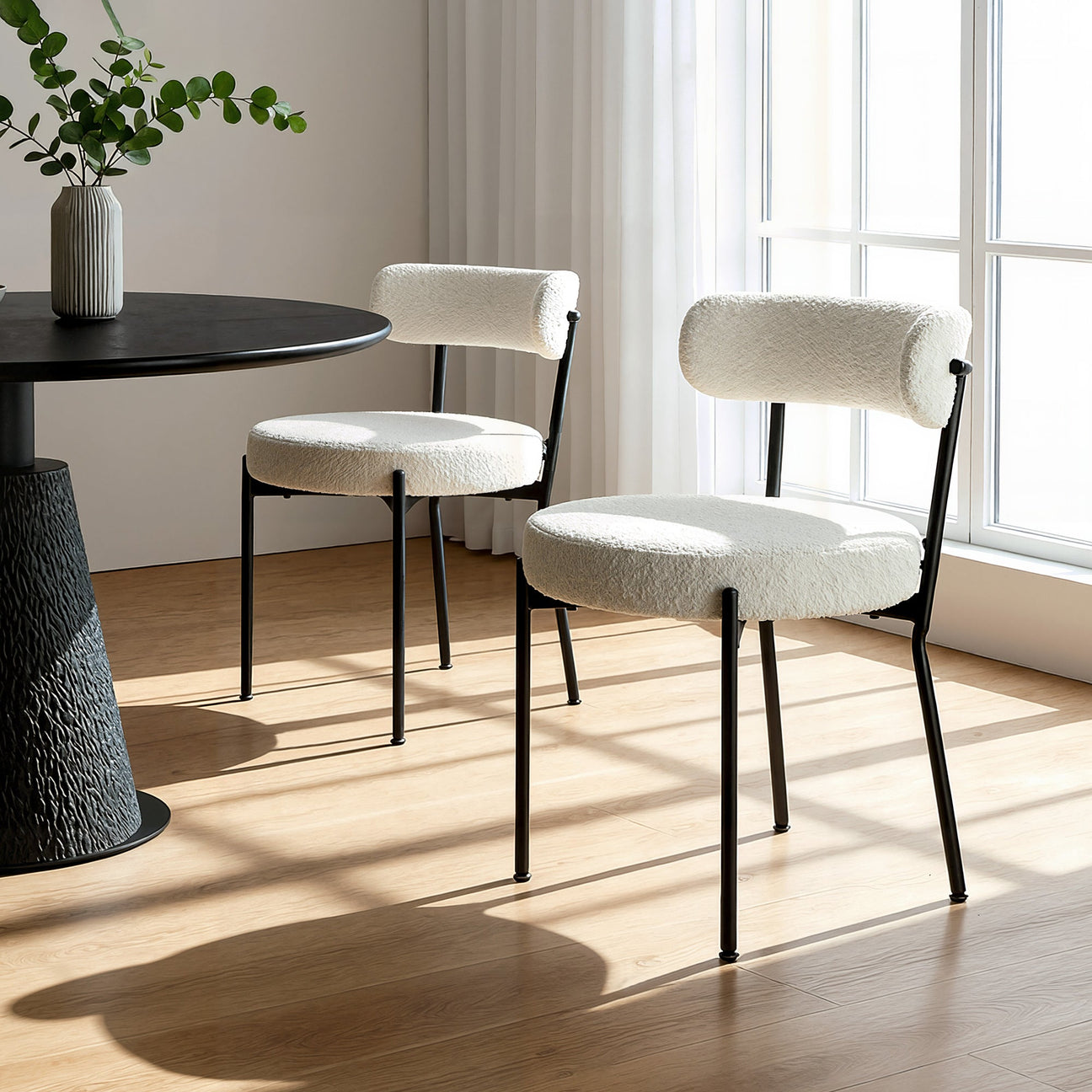 Modern dining chairs with white cushioned seats in a bright room with large windows.