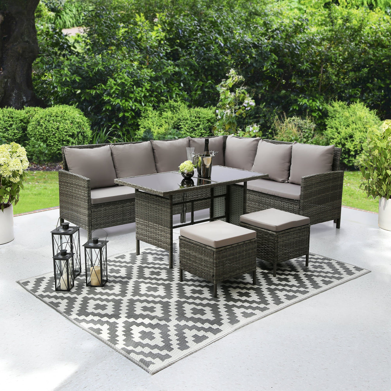 Outdoor patio furniture set with table and chairs on a patterned rug in a garden setting.
