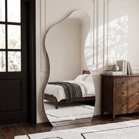 Lesina Frameless Full Length Pond Mirror styled in a bedroom beside a wooden chest of drawers.