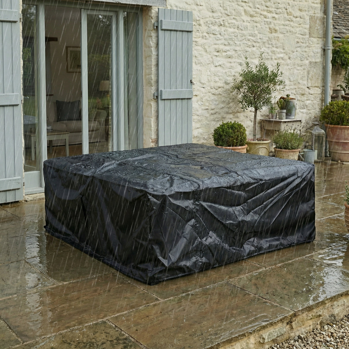 Outdoor furniture cover protecting a table on a stone patio with a stone building in the background.