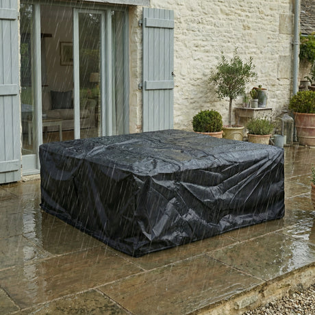 Outdoor furniture cover protecting a table on a stone patio with a stone building in the background.