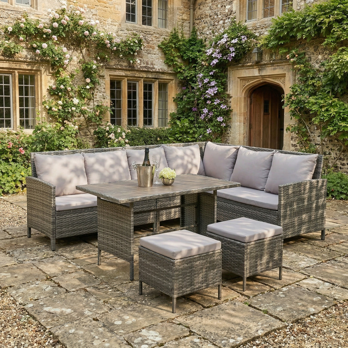 Outdoor patio set with gray cushions in front of a stone building with greenery.